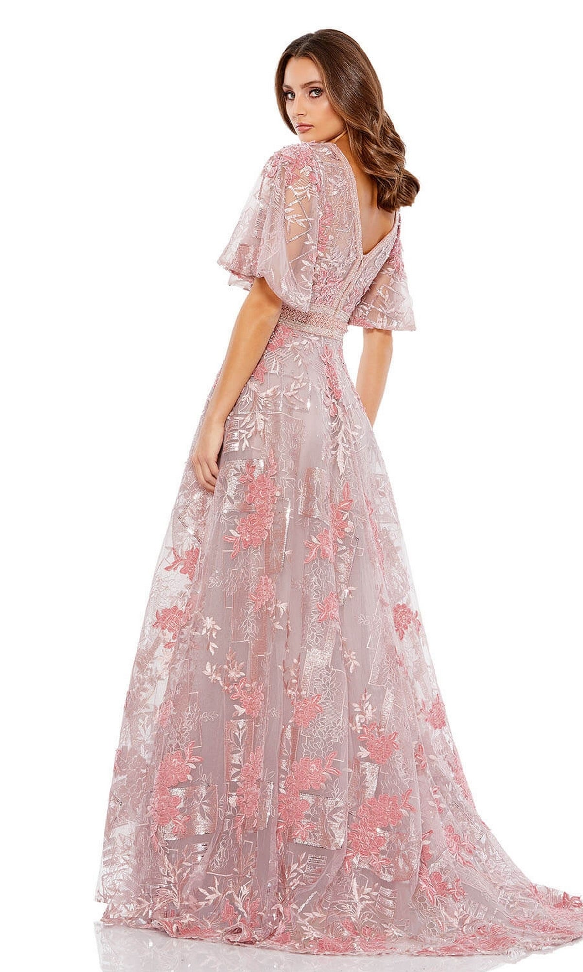 Woman wearing the Long Formal Dress 20262 by Mac Duggal, a floor-length pink A-line gown with floral embroidery, flounce sleeves, deep V-neckline, and V-back, standing and looking over her shoulder.